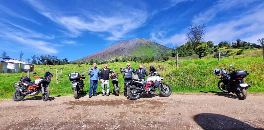 Groupe de riders Pura Vida Motorbike devant un volcan, sous le ciel bleu